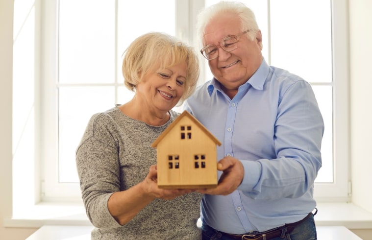 Happy elderly couple holding miniature house