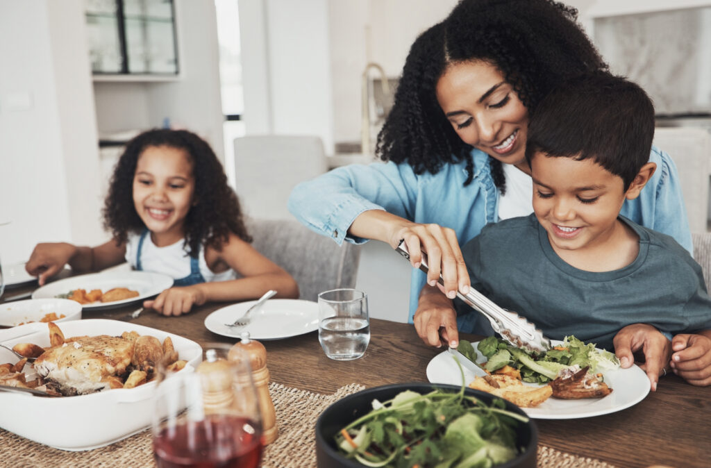 Mom, children and eating food in home together for lunch, dinner table and healthy meal. Happy family, mother and kids smile for dining in house with love, care and happiness of delicious supper