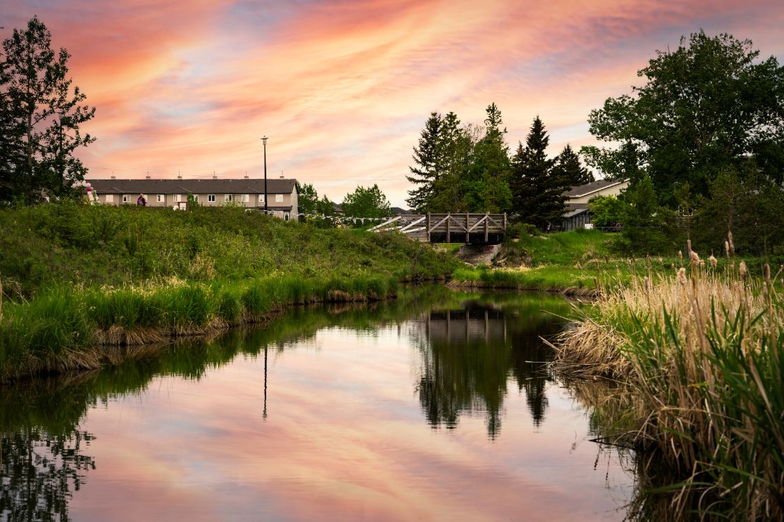 Ruisseau avec passerelle et maisons au coucher du soleil à Airdrie, en Alberta