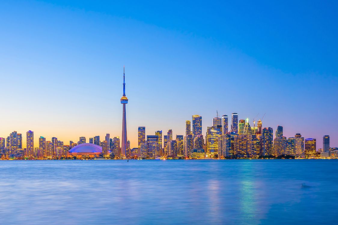 L'horizon de Toronto au crépuscule, avec la Tour CN et les lumières des gratte-ciel se reflétant sur le lac Ontario.