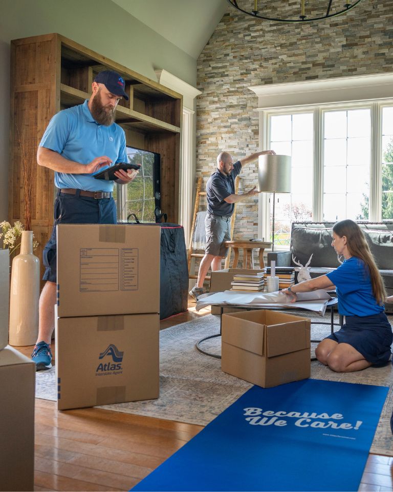 A man and woman are carrying boxes into a living room, preparing to organize their new space.