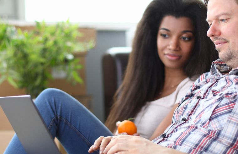 A man and woman sit together on a couch, using a laptop.